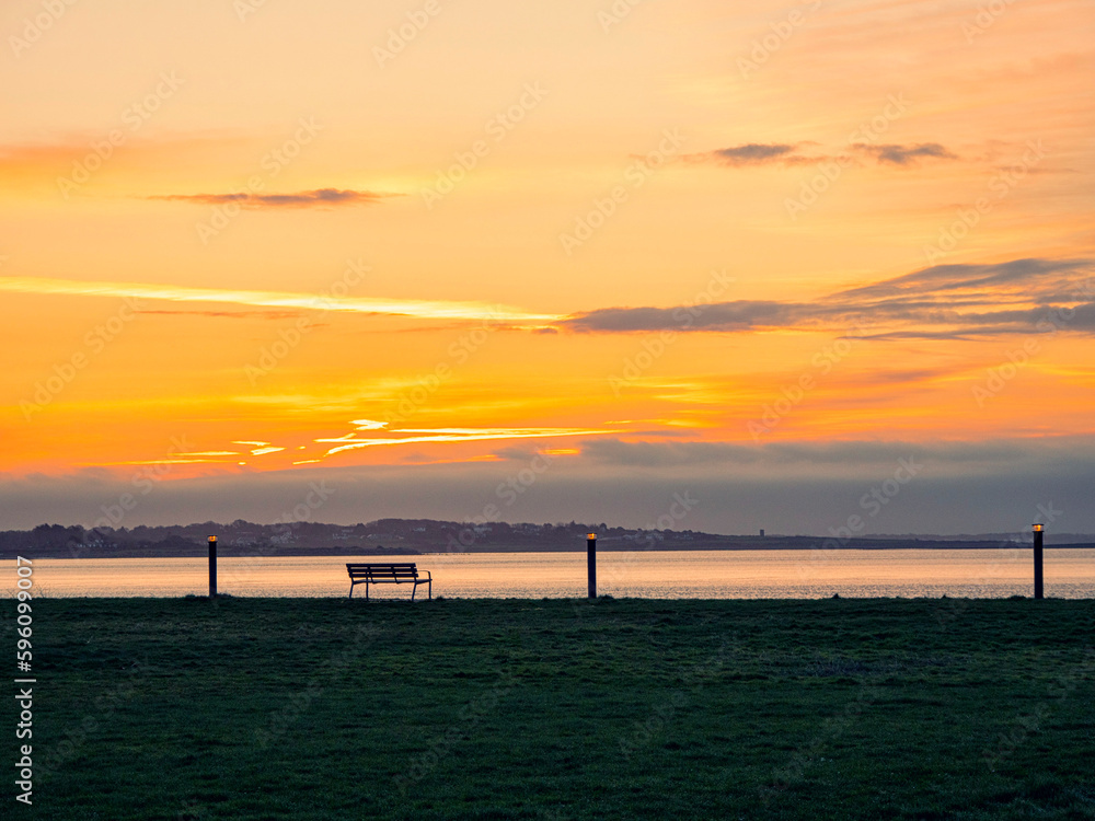 Obraz premium Empty bench by the ocean at sunrise. Warm and cool color.