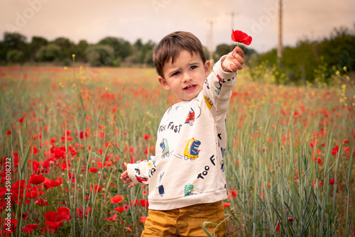 Fototapete Niño feliz cogiendo flores en un campo de amapolas rojas