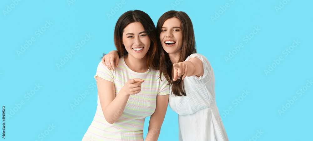 Young gossiping women pointing at viewer on light blue background Young gossiping women pointing at viewer on light blue background