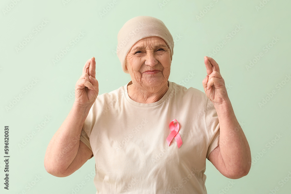 Senior woman after chemotherapy with pink ribbon crossing fingers on green background. Breast cancer concept Senior woman after chemotherapy with pink ribbon crossing fingers on green background. Breast cancer concept