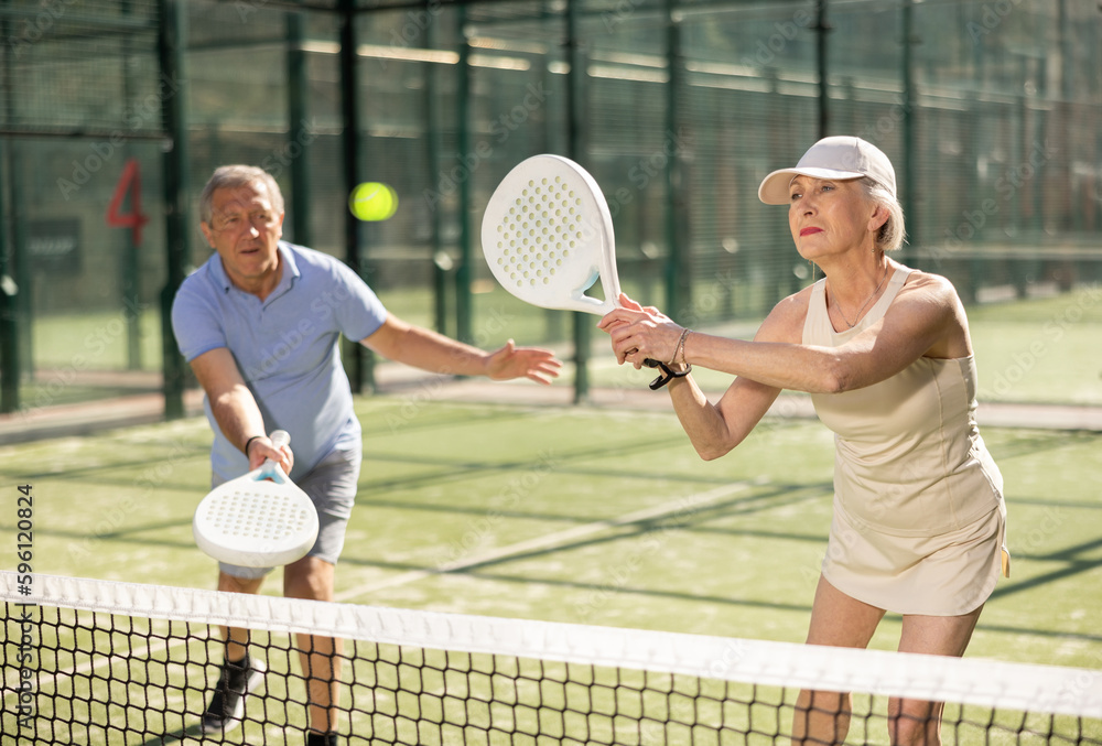 Fototapeta premium Mature sporty mature couple playing padel game in court on sunny day