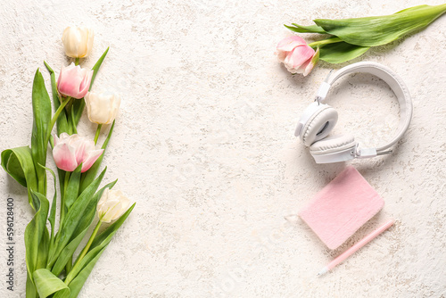 Modern headphones, notebook and beautiful tulip flowers on light background