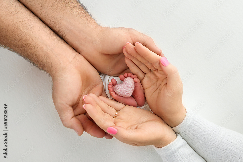 Feet, toes, heels of a newborn. Children's foot in the hands of mother, father, parents with a knitted pink heart. The legs of the child in the arms of mom and dad. On a white background.