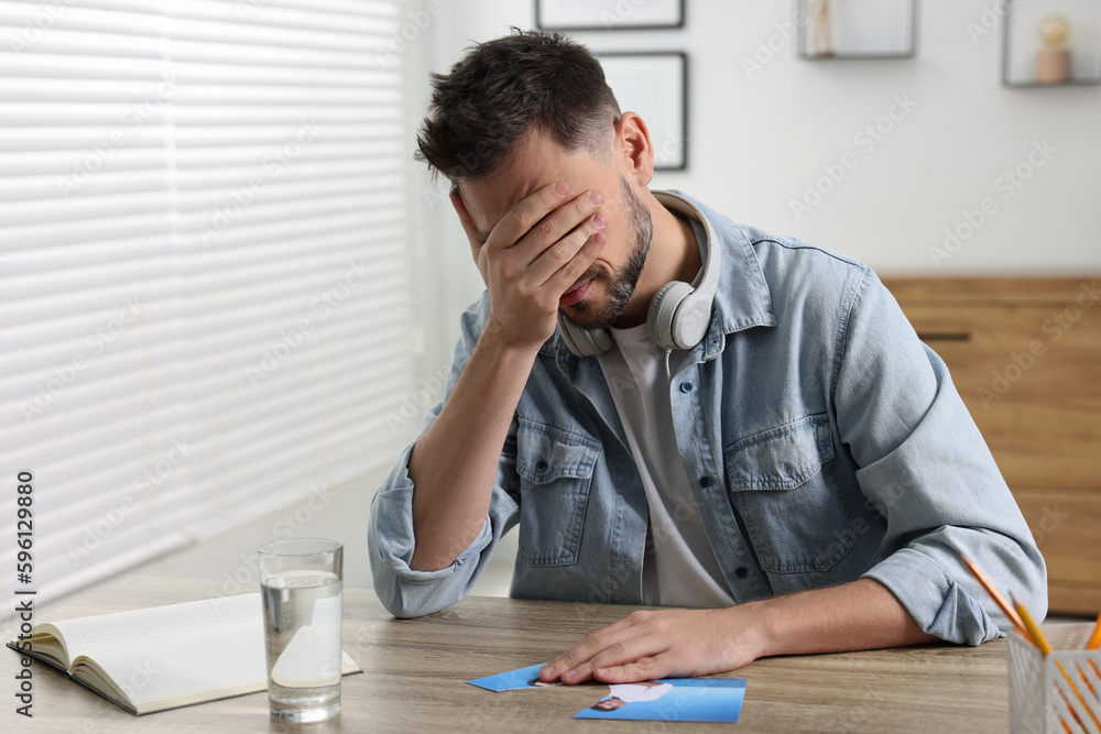 Crying man with parts of photo sitting at table indoors. Divorce concept Crying man with parts of photo sitting at table indoors. Divorce concept