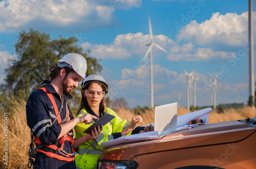 Two professional maintenance engineers in safety workwear using laptop and tablet checklist wind turbine on windmill construction farms.