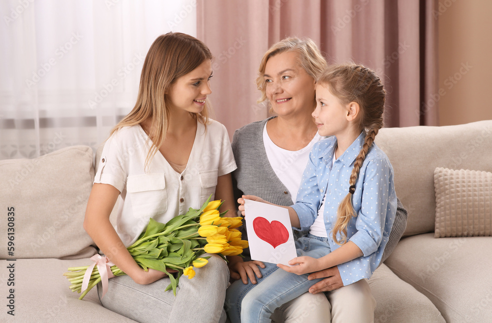 Little girl congratulating her mom and granny with flowers and postcard at home. Happy Mother's Day