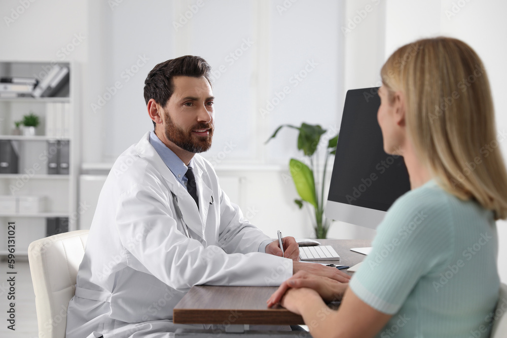 Doctor consulting patient at wooden table in clinic Doctor consulting patient at wooden table in clinic