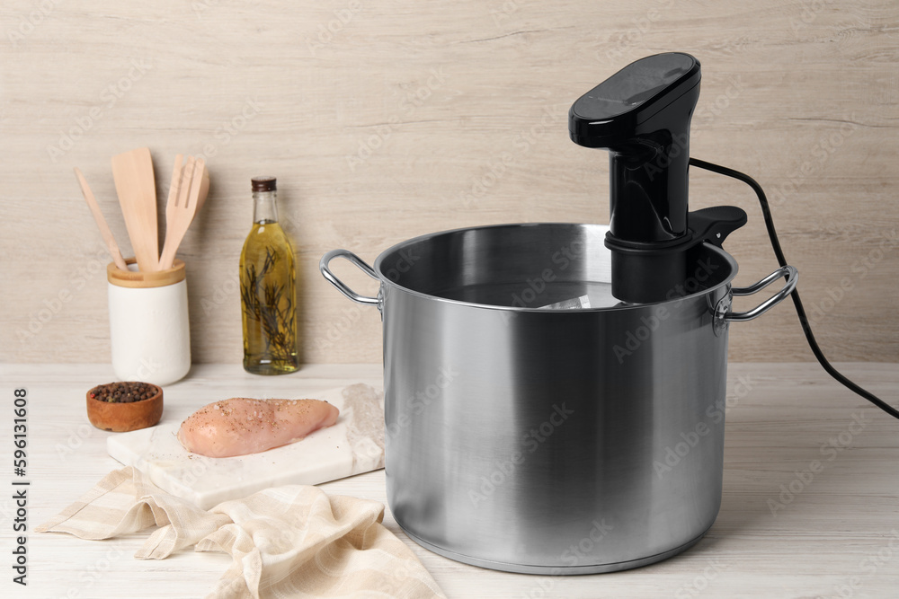 Thermal immersion circulator in pot and meat on white wooden table. Sous vide cooking Thermal immersion circulator in pot and meat on white wooden table. Sous vide cooking