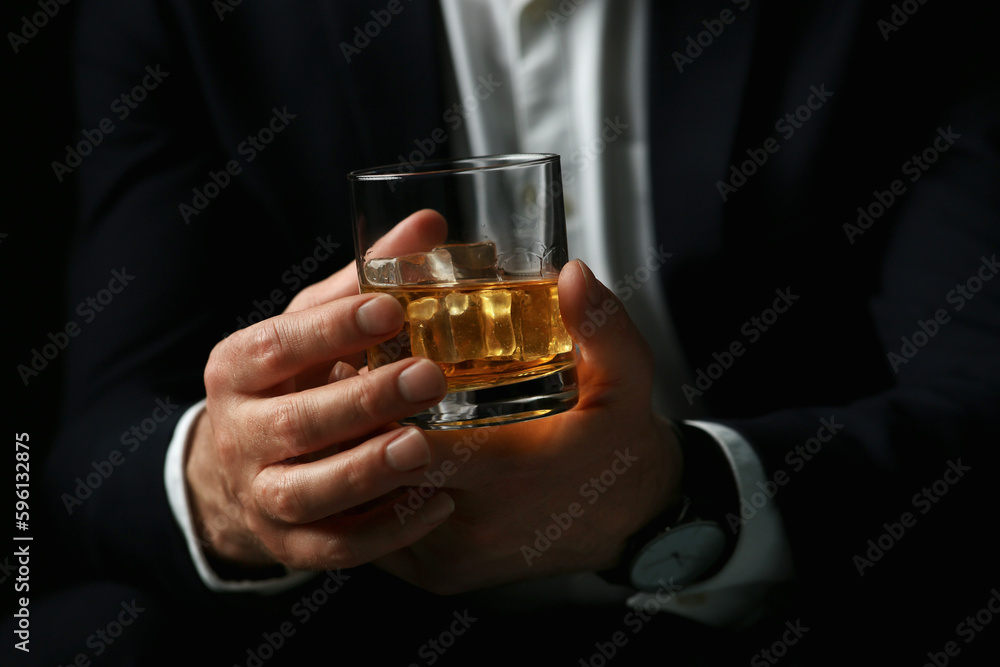 Man holding glass of whiskey with ice cubes on black background, closeup Man holding glass of whiskey with ice cubes on black background, closeup