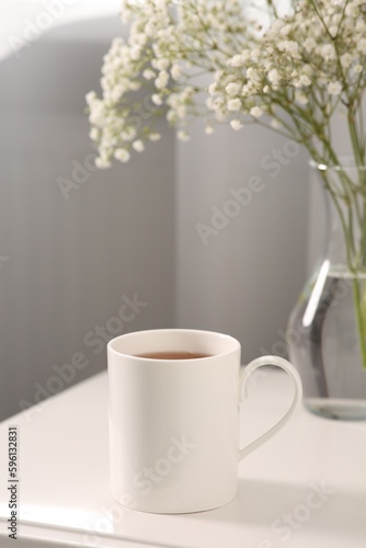 Ceramic mug with tea on white bedside table indoors. Mockup for design