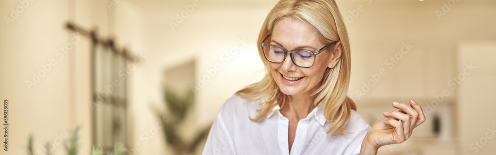 Attractive mature businesswoman smiling and making notes while having online video call using laptop, sitting at her desk in the office Attractive mature businesswoman smiling and making notes while having online video call using laptop, sitting at her desk in the office