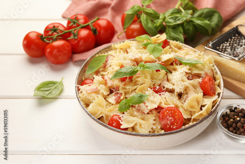 Plate of delicious pasta with tomatoes, basil and parmesan cheese on white wooden table