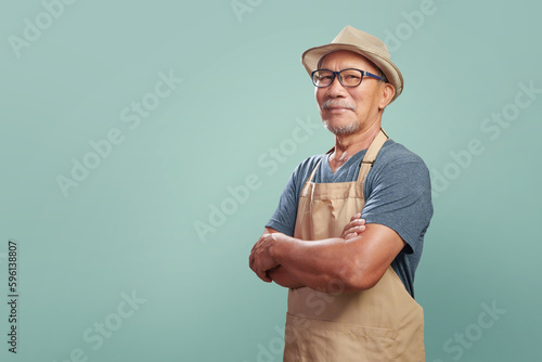 Portrait of Asian Senior man wearing brown apron smiling with arms crossed over isolated color background, Small business owner, Entrepreneur