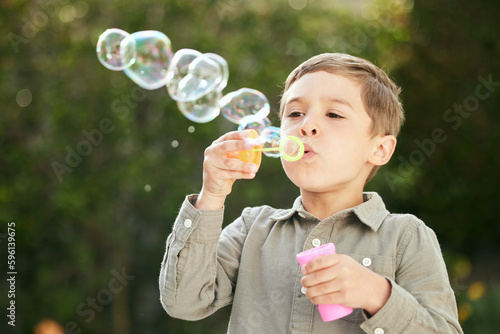 Give a child bubbles and theyll be entertained. an adorable little boy blowing bubbles outside.