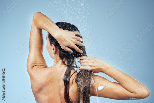 Rinsing all the shampoo out of her hair. Studio shot of an attractive young woman washing her hair while taking a shower against a blue background.