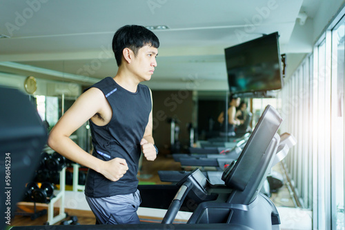 Active Asian sportsman making a cardio exercise by running on the treadmill machine in a fitness or gym  healthy sport man doing a cardio workout.
