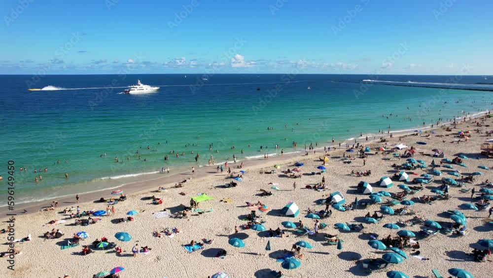 Drone clip over busy golden beach with people sunbathing and colourful umbrellas, with blue green open sea and cruise ship in the background Drone clip over busy golden beach with people sunbathing and colourful umbrellas, with blue green open sea and cruise ship in the background