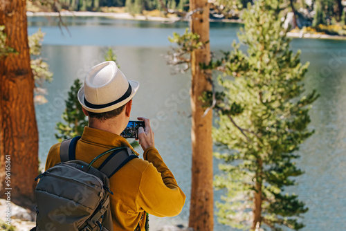 Man with a backpack taking picture of a peaceful mountain fall lake on a sunny day