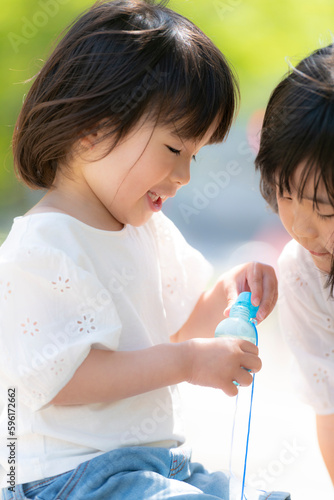 新緑の初夏の公園で遊ぶ小さな姉妹