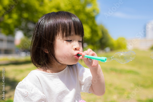 新緑の初夏の公園でシャボン玉をして遊ぶ小さな女の子