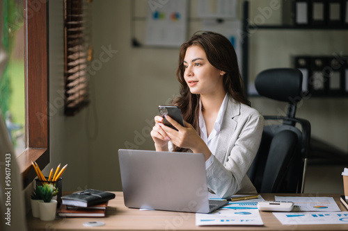 Confident business expert attractive smiling young woman typing laptop ang holding digital tablet  on desk in office..