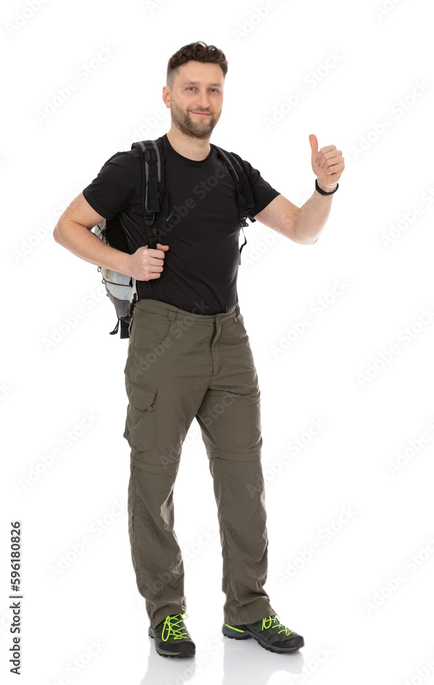 Full length portrait of happy hiker with a backpack showing thumbs up gesture, isolated on white background. Thirty years old man smiling and posing in studio. Full length portrait of happy hiker with a backpack showing thumbs up gesture, isolated on white background. Thirty years old man smiling and posing in studio.