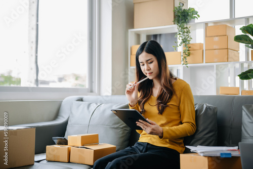 .Young business owner woman prepare parcel box and standing check online orders for deliver to customer on tablet, laptop Shopping Online concept.