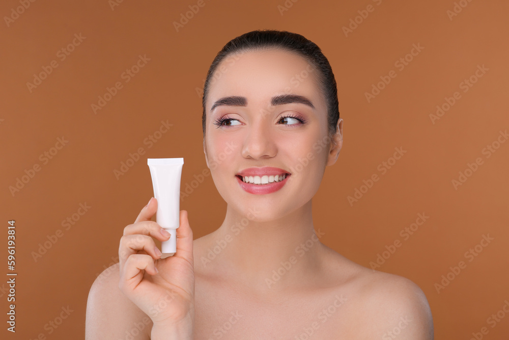 Woman holding tube of foundation on brown background Woman holding tube of foundation on brown background