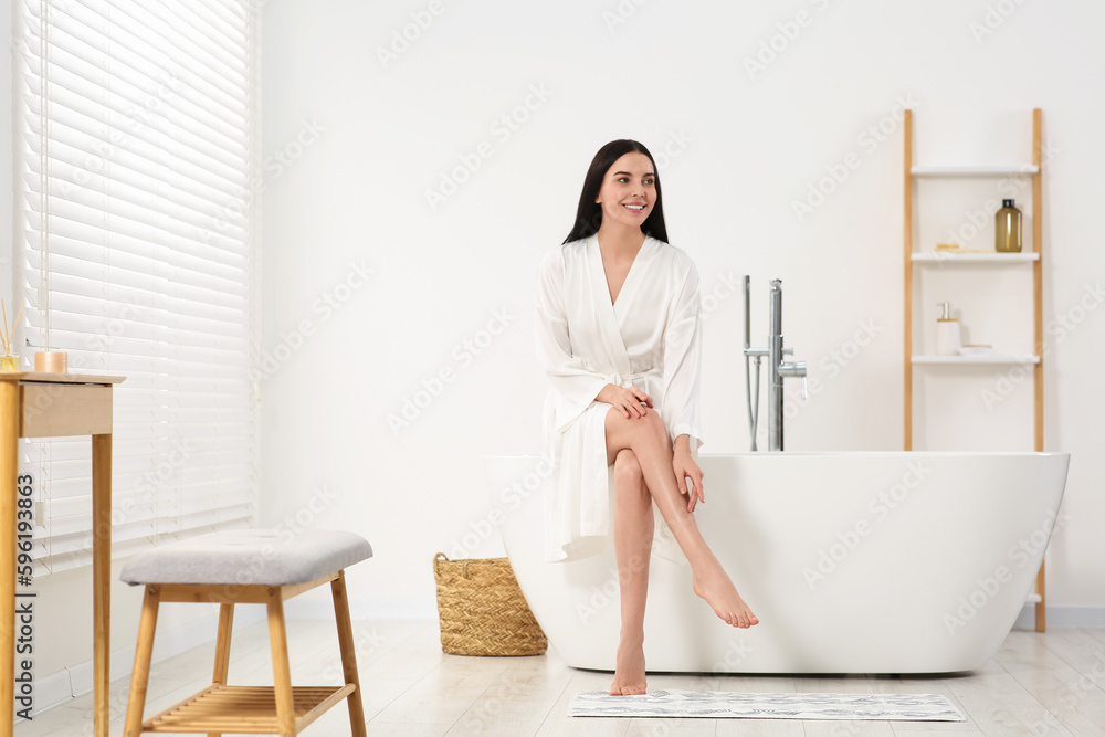 Beautiful happy woman in stylish bathrobe sitting on tub in bathroom - obrazy, fototapety, plakaty 