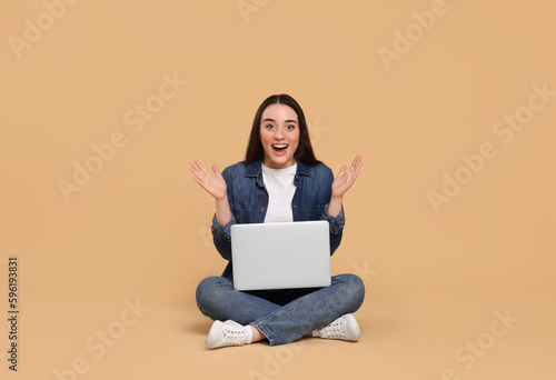 Happy young woman with laptop on beige background