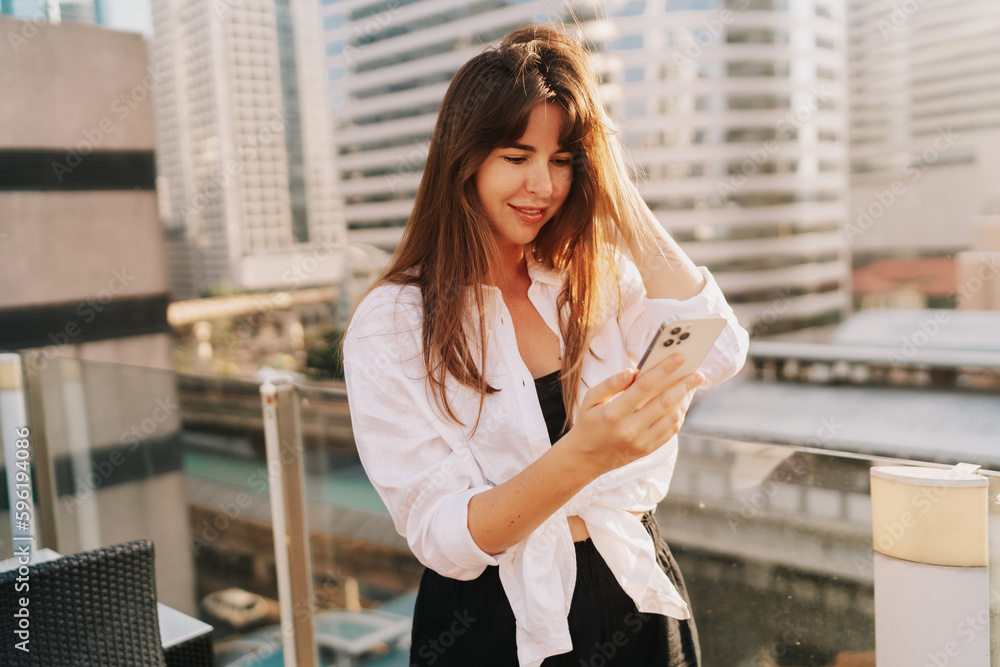 Fototapeta premium Pretty brunette woman using mobyle phone while walking in Bangkok. Modern architecture on background.