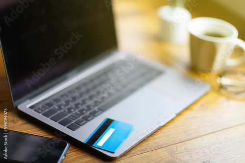 credit card lying on laptop computer, next cup of coffee, reading glasses, mobile phone. Online shopping, e-commerce, internet banking, spending money, working from home concept