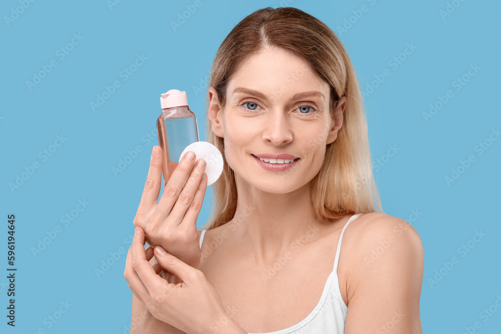 Beautiful woman with makeup remover and cotton pad on light blue background Beautiful woman with makeup remover and cotton pad on light blue background