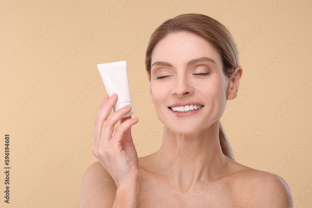 Woman holding tube of foundation on beige background Woman holding tube of foundation on beige background