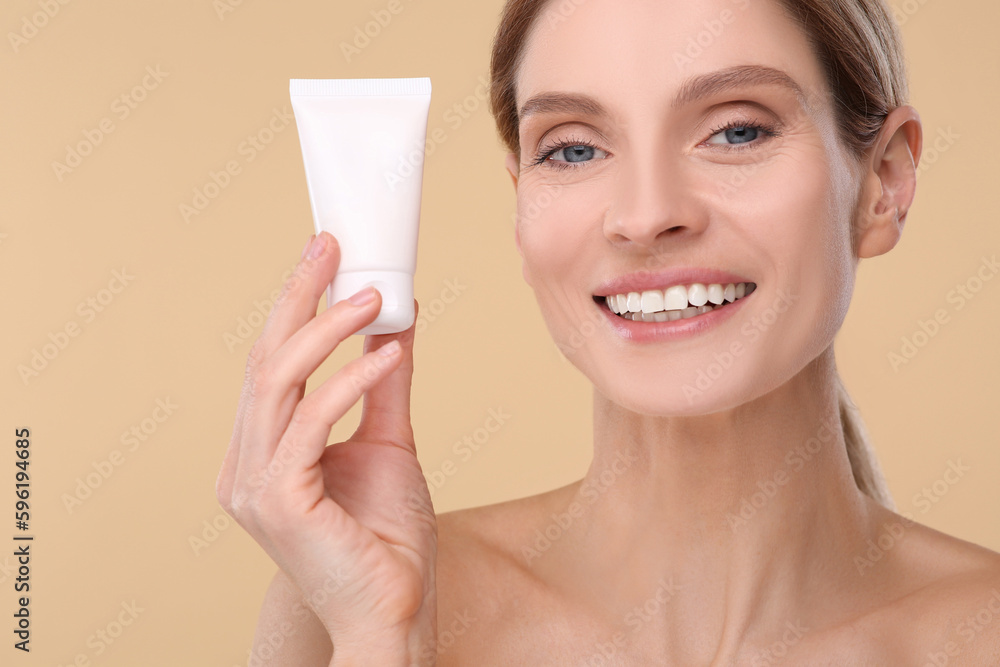 Woman holding tube of foundation on beige background Woman holding tube of foundation on beige background