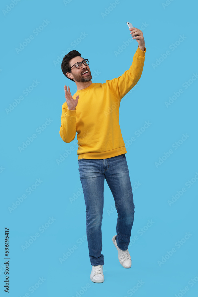 Smiling man taking selfie with smartphone on light blue background Smiling man taking selfie with smartphone on light blue background