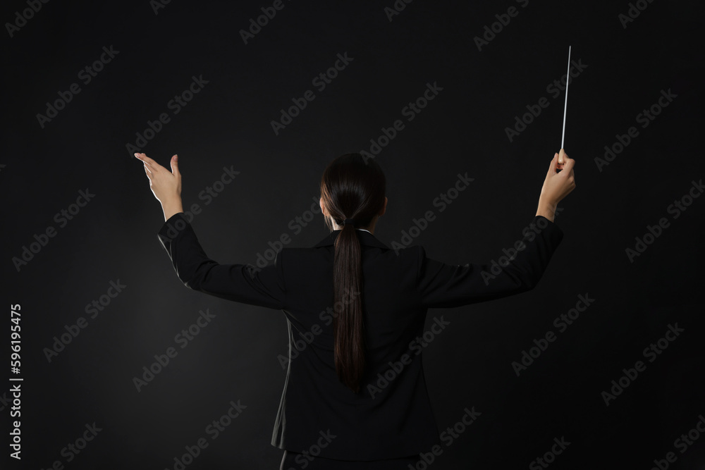 Professional conductor with baton on dark background, back view Professional conductor with baton on dark background, back view