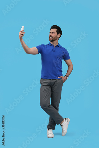 Smiling man taking selfie with smartphone on light blue background