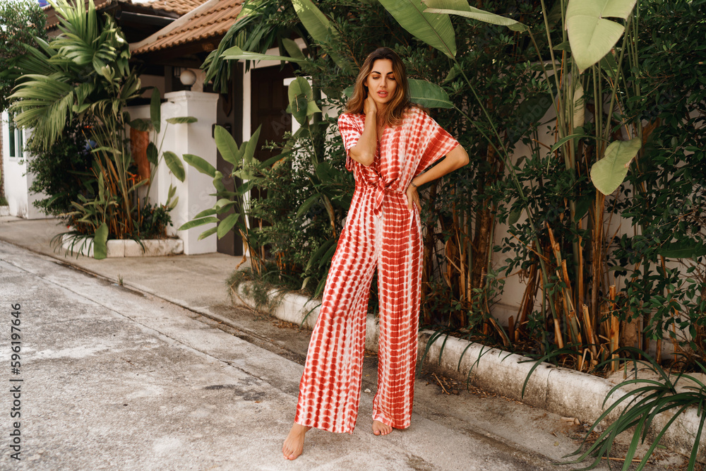 Outdoor fol lenght photo brunette young woman posing near palm trees and wearing modern trendy outfit . tropical vacation mood. Outdoor fol lenght photo brunette young woman posing near palm trees and wearing modern trendy outfit . tropical vacation mood.