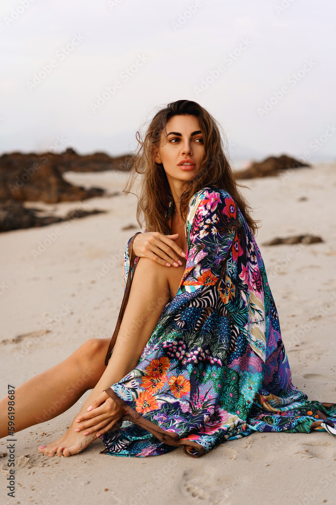 portrait of beautiful brunette woman in sexy swimwear and boho cimono with tropical print posing on the beach in sunset light. Prtfect wavy hairs, tan skim body. portrait of beautiful brunette woman in sexy swimwear and boho cimono with tropical print posing on the beach in sunset light. Prtfect wavy hairs, tan skim body.