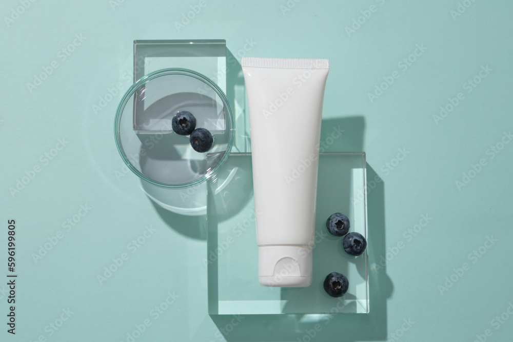 Top view of cosmetics tube mockup for design placed on transparent podiums, blueberries and essence on petri dish display on blue background. Scene for promote cosmetic, copy space Top view of cosmetics tube mockup for design placed on transparent podiums, blueberries and essence on petri dish display on blue background. Scene for promote cosmetic, copy space
