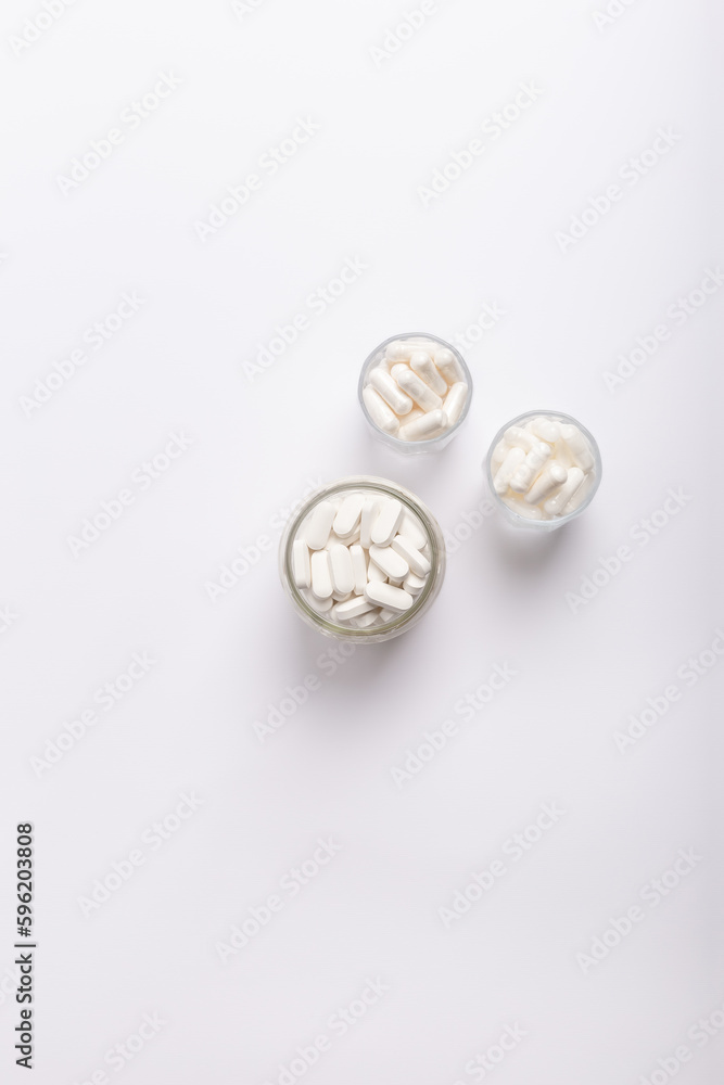 Organic food supplements, vitamins and minerals in glass jars from above on white background. 