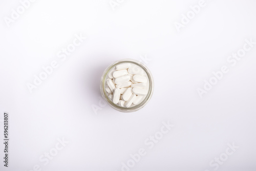 White tablets in glass transparent jar on white background. 