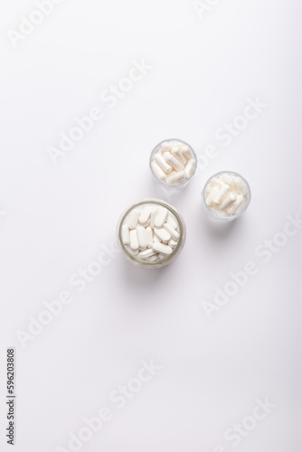 Organic food supplements, vitamins and minerals in glass jars from above on white background. 