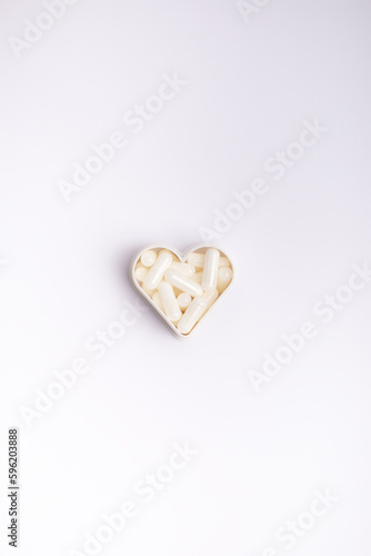 White capsules in heart shaped form on white background from above. Vitamins and minerals.