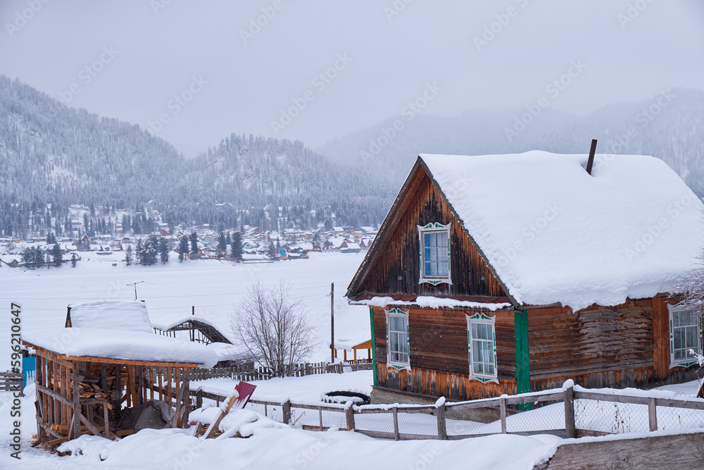 Old wooden house. The roof is covered with a thick layer of snow. Altai village Artybash in winter season.