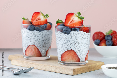 Chia pudding with strawberries and blueberries, chia seeds on a pink background. Healthy breakfast rich in protein - chia seed pudding, coconut milk and strawberries.