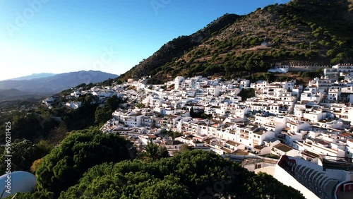 Drone clip of white and terracotta buildings in Mijas Pueblo, surrounded by thick forested mountain slopes on a sunny day