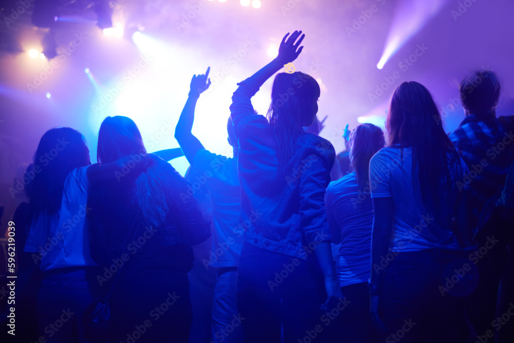 Purple, neon light and people dancing at music festival from back, night and energy at live concert event. Dance, fun and group of excited fans in arena at rock band performance or crowd at party.