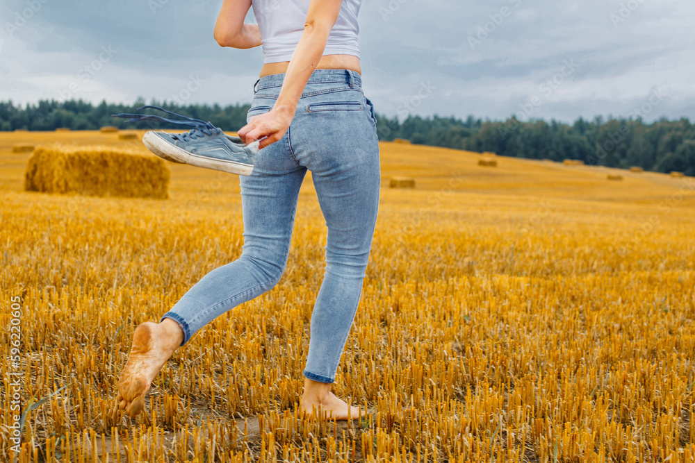 barefoot girl with sneakers in hand walking in the agricultural field with haystack and bales barefoot girl with sneakers in hand walking in the agricultural field with haystack and bales